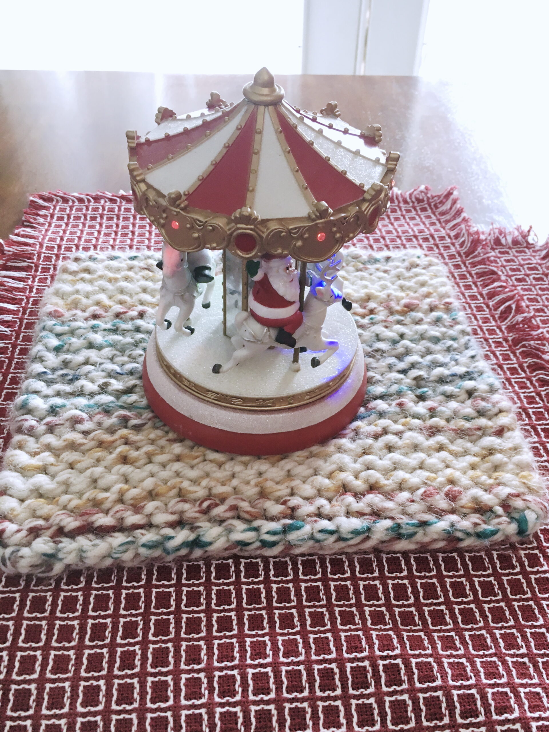 Using the Cherry Candy Cane Potholder as a decorative Christmas accent under a miniature Santa carousel toy. Get the pattern free from Liz Chandler @PurlsAndPixels.