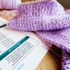 Knitting troubleshooter printed and laid on a wooden table next to a purple ribbed scarf.
