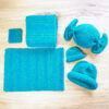 Kids' knitting projects on wooden table - coaster, placemat, scarf, hats, and a candy toy knitted in blue and teal super-bulky yarn.