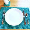 Super-Bulky knit placemat on wooden table with white plate and silverware next to matching knit coaster and mug.