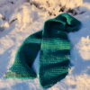 A teal super bulky knit scarf laid haphazardly in fresh snow.
