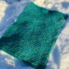Finished teal super-bulky knit placemat posed haphazardly in the snow.