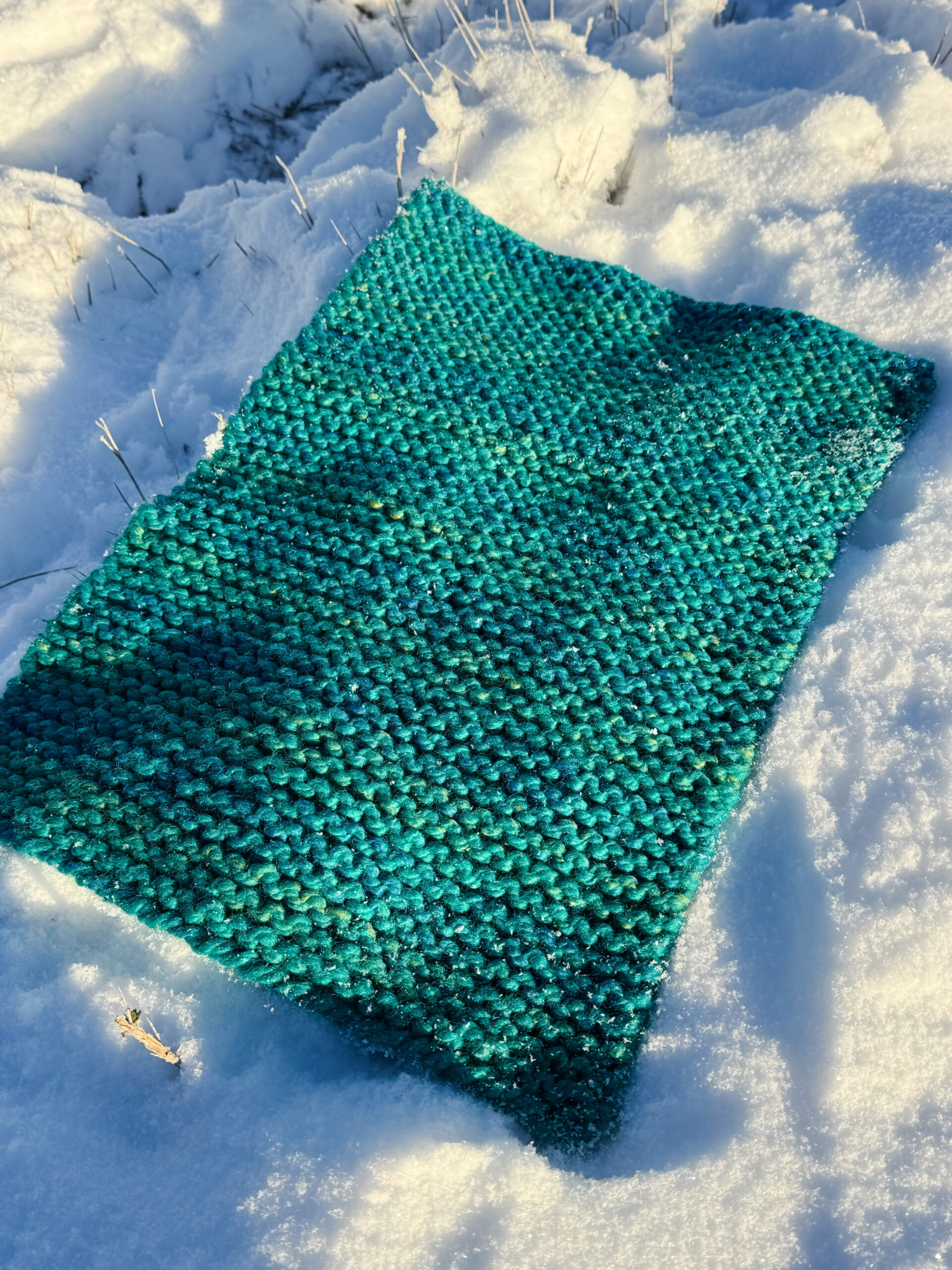 Finished teal super-bulky knit placemat posed haphazardly in the snow.