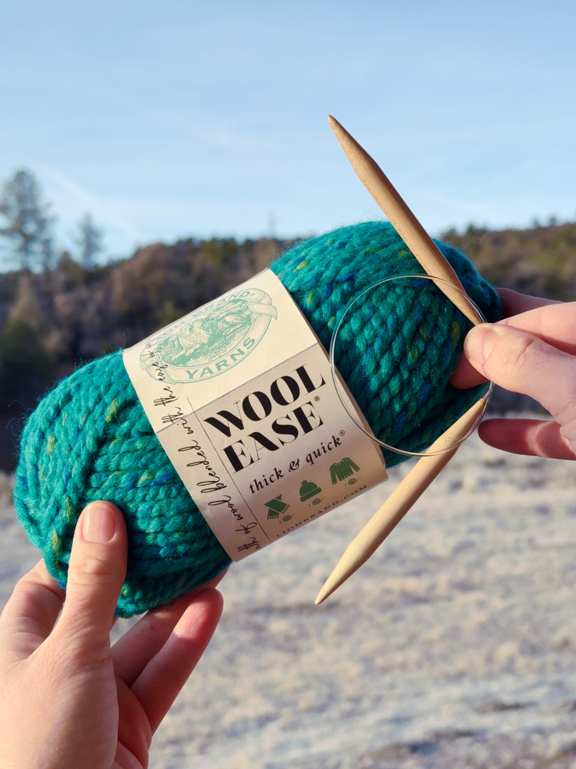 Kids' knitting lessons start with super-bulky yarn and US No. 13 needles, shown here outside held in front of a blue sky.