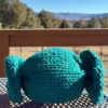 Knitted candy pillow toy finished in super-bulky blue yarn on a purple porch table.