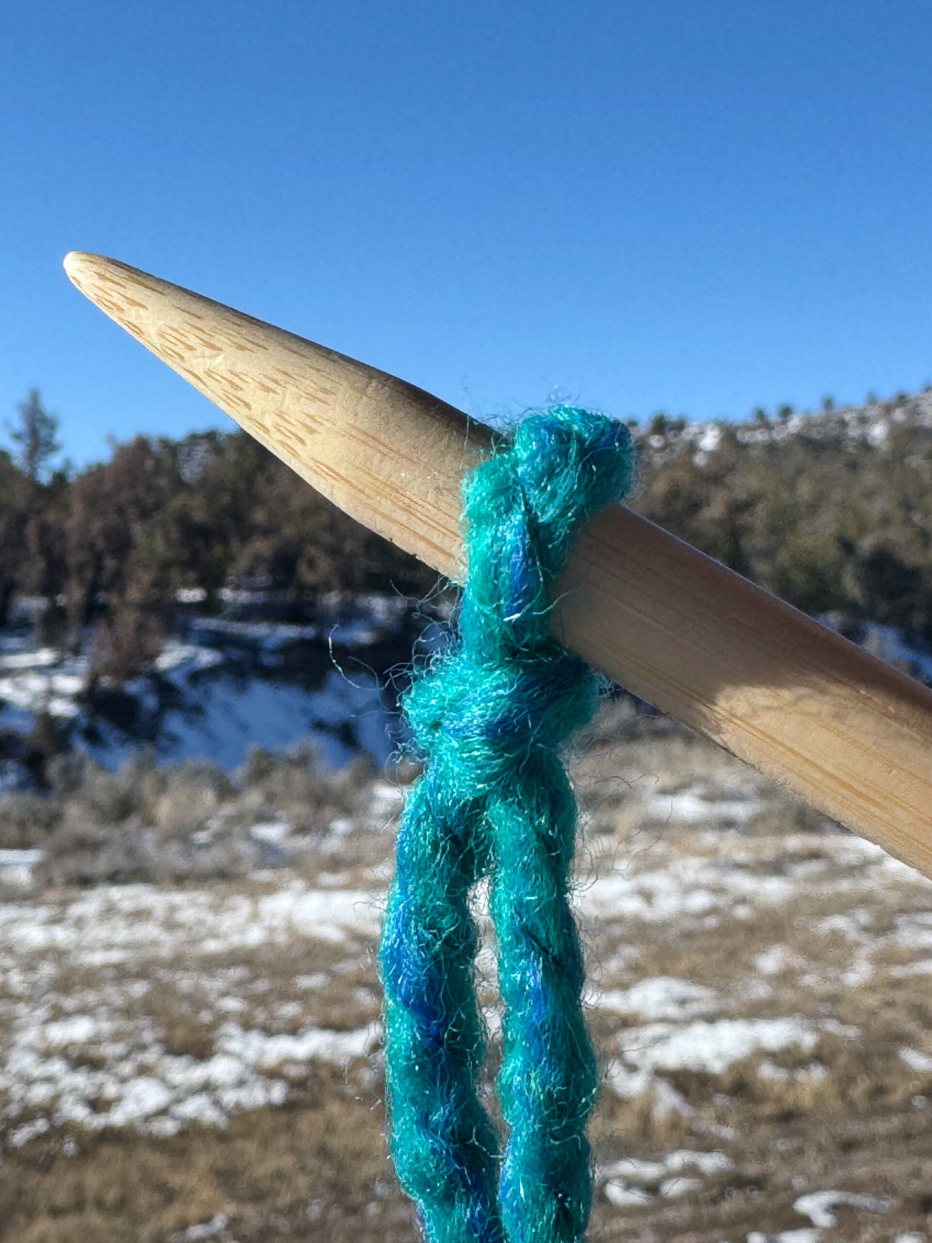 Closeup of the tip of a knitting needle with a slipknot looped onto it.