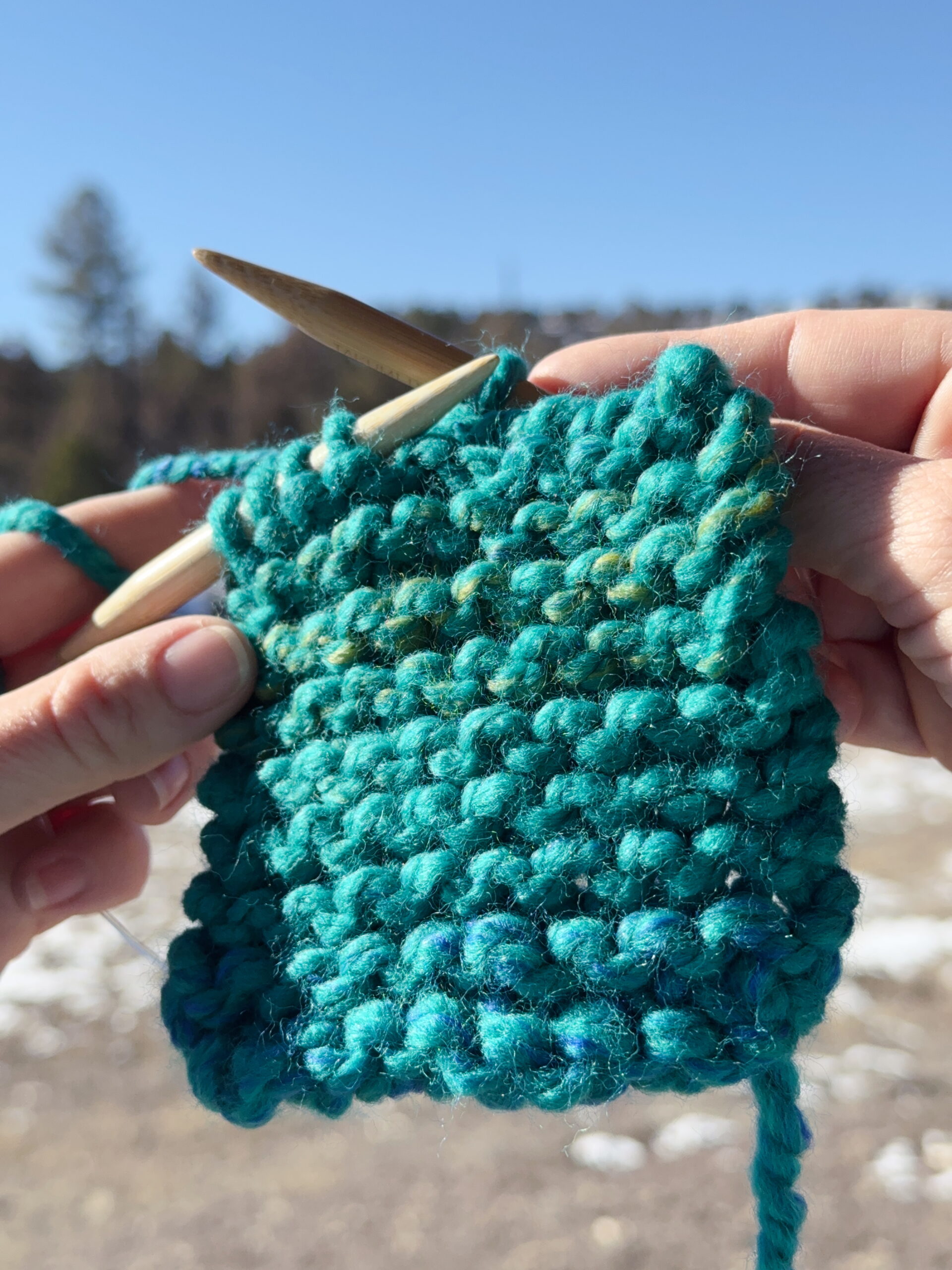 Hands showing a partially finished knitted bind off on a beginner knitting project.