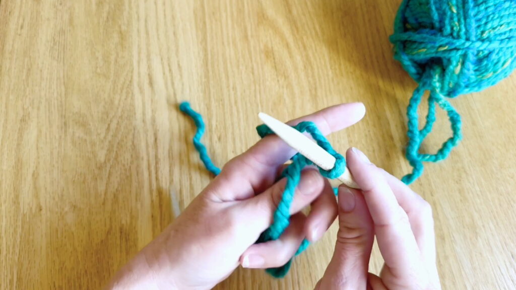 Left hand closed over the yarn with the last three fingers holding the yarn strands.