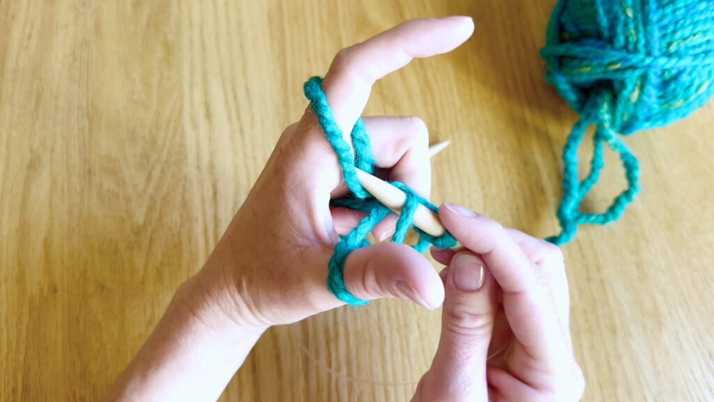 Needle tip moving over the next two yarn strands toward the palm during the cast on.
