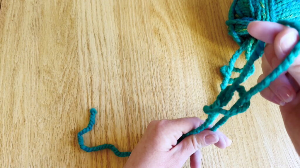 Hands pulling the yarn ends to tighten the knot at the bottom of the loop.