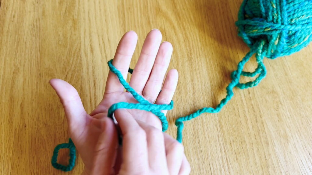 Yarn wrapped around the left hand with the tail crossing over the palm.