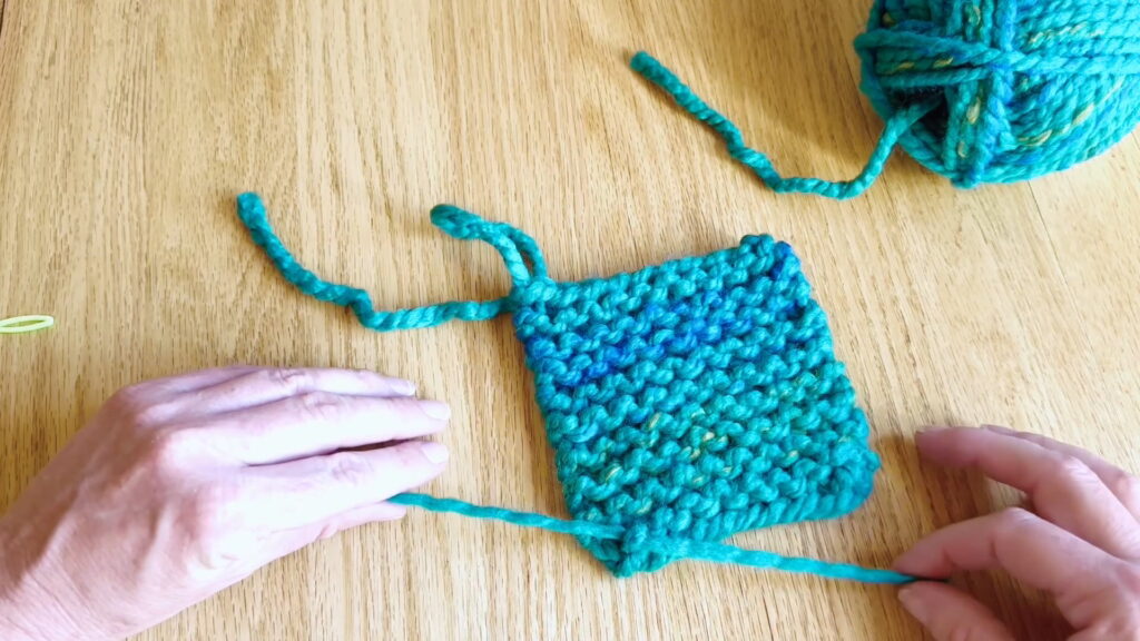 Pulling the yarn knots tight so the loose ends stay secure in the finished knitting project.