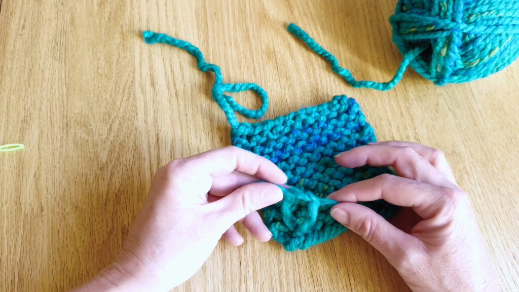 Tying a second securing knot in the yarn ends to prevent unraveling in beginner knitting.