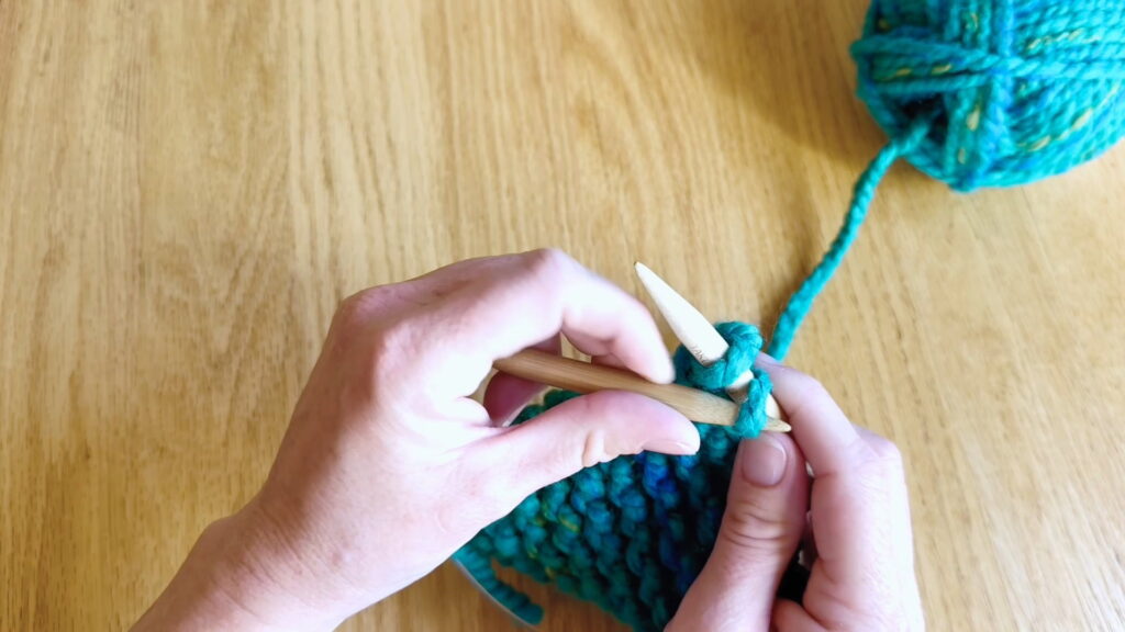 Knitting the next stitch to continue binding off stitches across the knitting row.