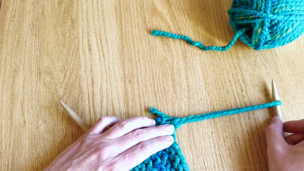 Pulling the final stitch larger to remove it from the needle and prepare to secure the yarn.