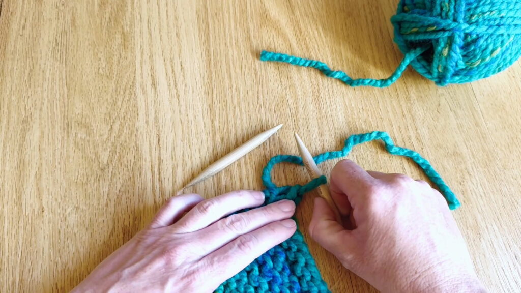 Holding the knitting project and needle near the last stitch before securing the final loop.