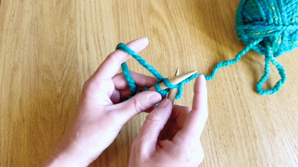 Right knitting needle inserted into the front of the first stitch on the left needle to begin a knit stitch.
