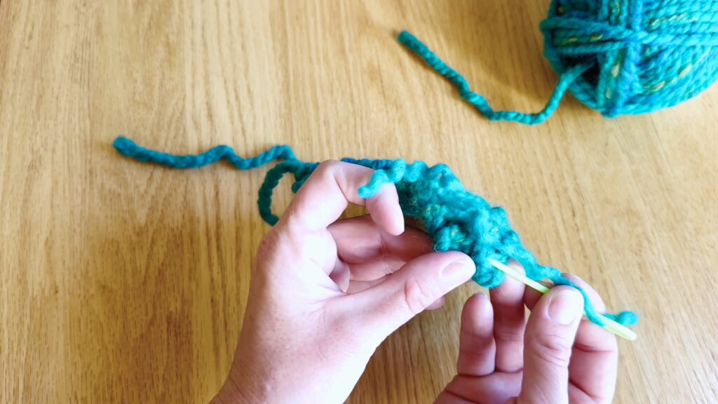 Sewing the split yarn tail around a knit stitch to anchor the loose end securely in beginner knitting.