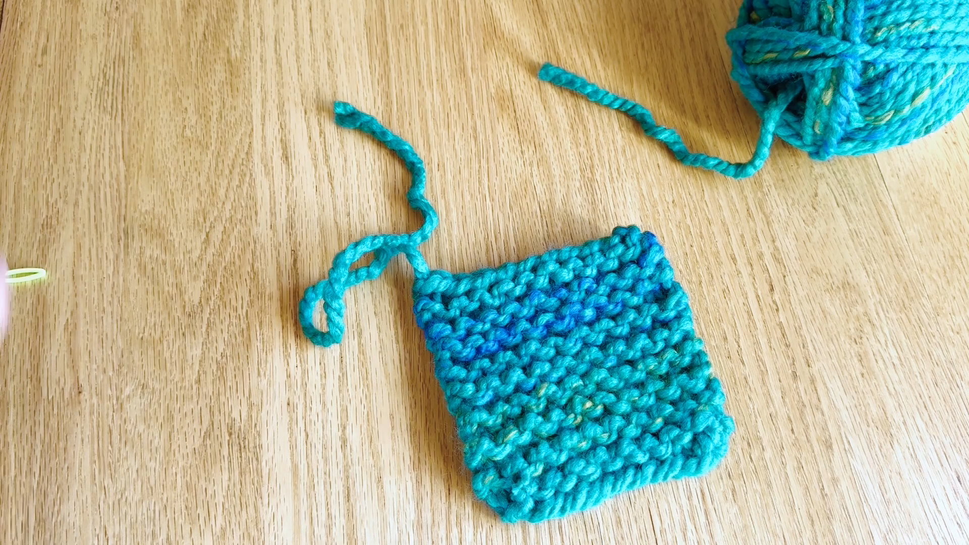Beginner knit coaster showing one loose yarn end woven into the fabric.