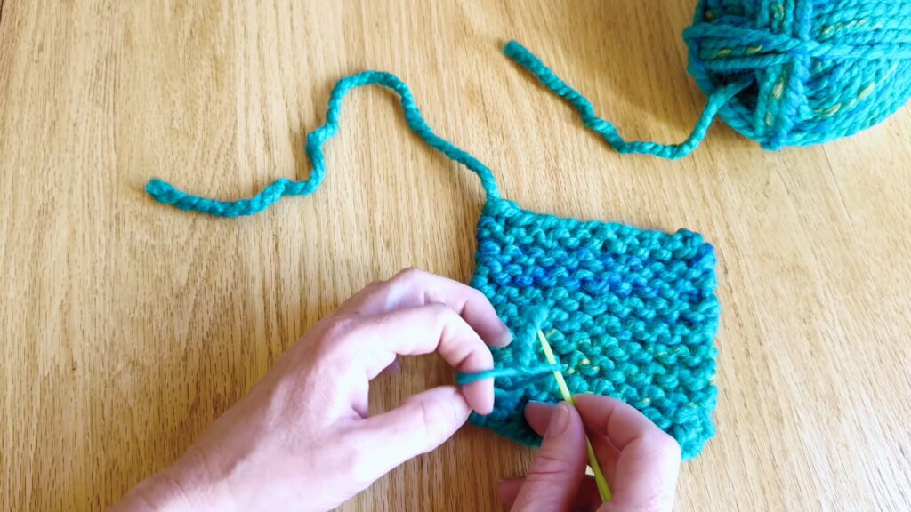 Splitting the yarn tail into two halves before anchoring the loose end in beginner knitting.