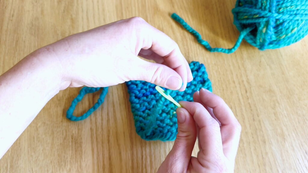 Threading a loose yarn end through the eye of a darning needle to begin weaving in loose ends in beginner knitting.