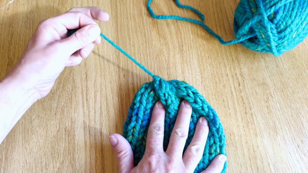 Lesson 9, Kids' Knitting Guide – pulling the yarn tight to close the top of a knitted hat.
