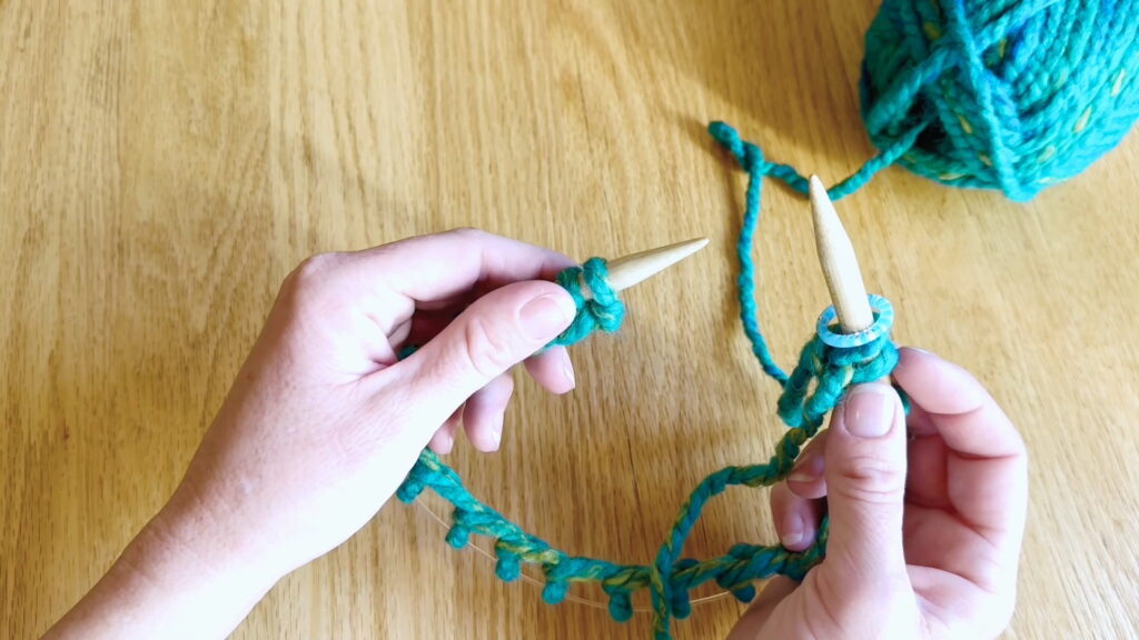 Lesson 8, Kids' Knitting Guide – sliding the first cast-on stitch to the tip of the needle before joining the round.