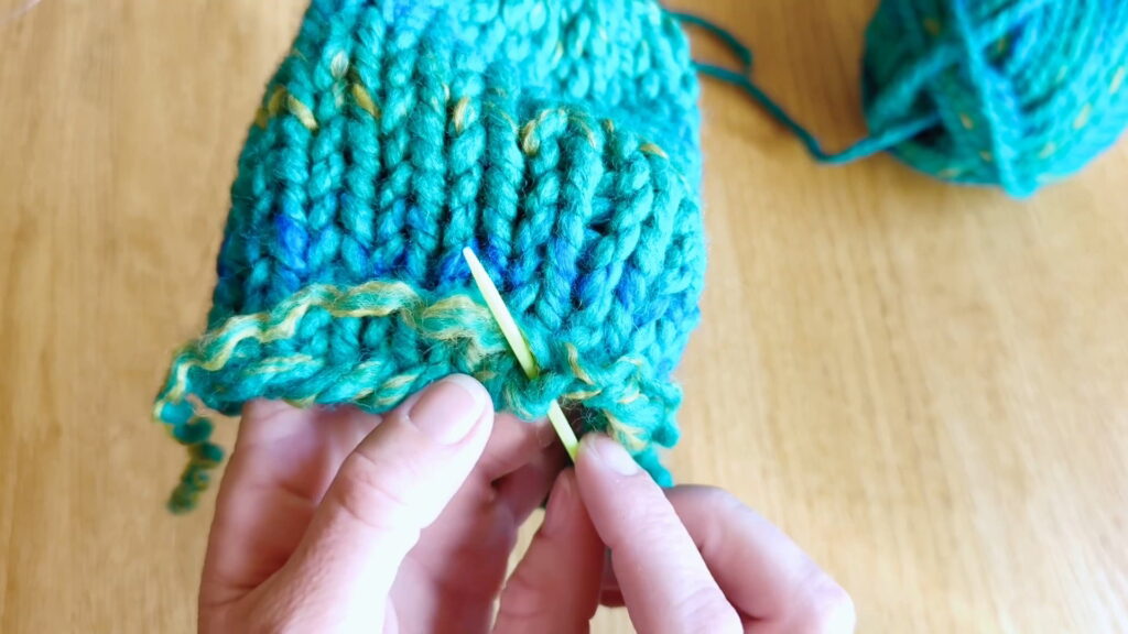 Lesson 10, Kids' Knitting Guide – anchoring split yarn to secure the bottom loose end of a knitted hat.