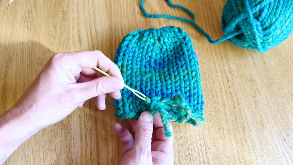 Lesson 10, Kids' Knitting Guide – anchoring a yarn tail into stitches near the brim of a knitted hat.