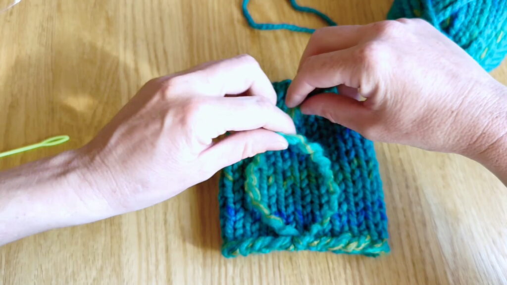 Lesson 10, Kids' Knitting Guide – holding yarn ends in opposite hands to tie a knot at the bottom of a hat.