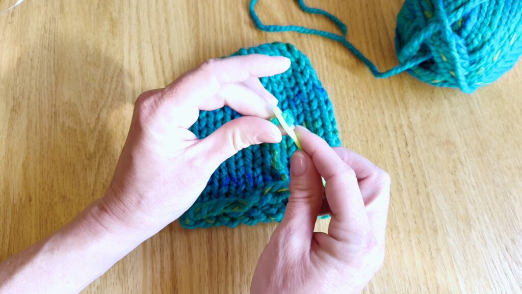 Lesson 10, Kids' Knitting Guide – threading yarn onto a darning needle to weave in the bottom loose end of a hat.