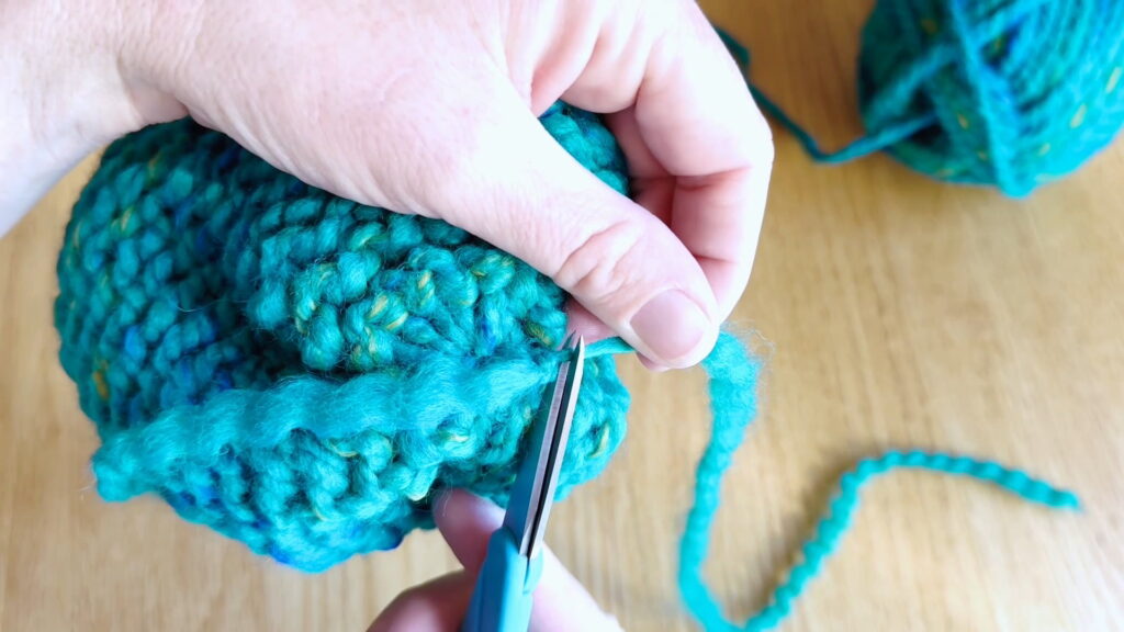 Lesson 10, Kids' Knitting Guide – trimming excess yarn after securing loose ends in a knitted hat.