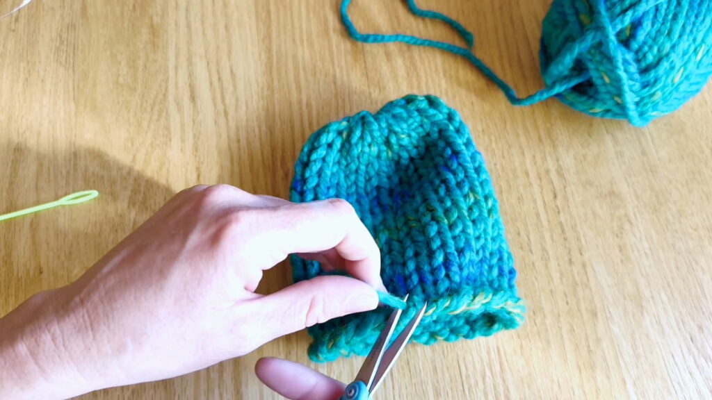 Lesson 10, Kids' Knitting Guide – trimming excess yarn after finishing the bottom loose end.