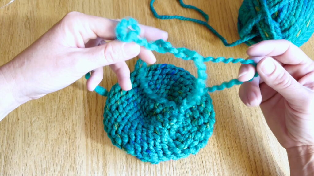 Lesson 10, Kids' Knitting Guide – tying the first knot to secure a yarn tail in a knitted hat.