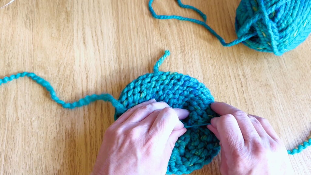 Lesson 10, Kids' Knitting Guide – pulling knots tight to secure loose ends in a knitted hat.